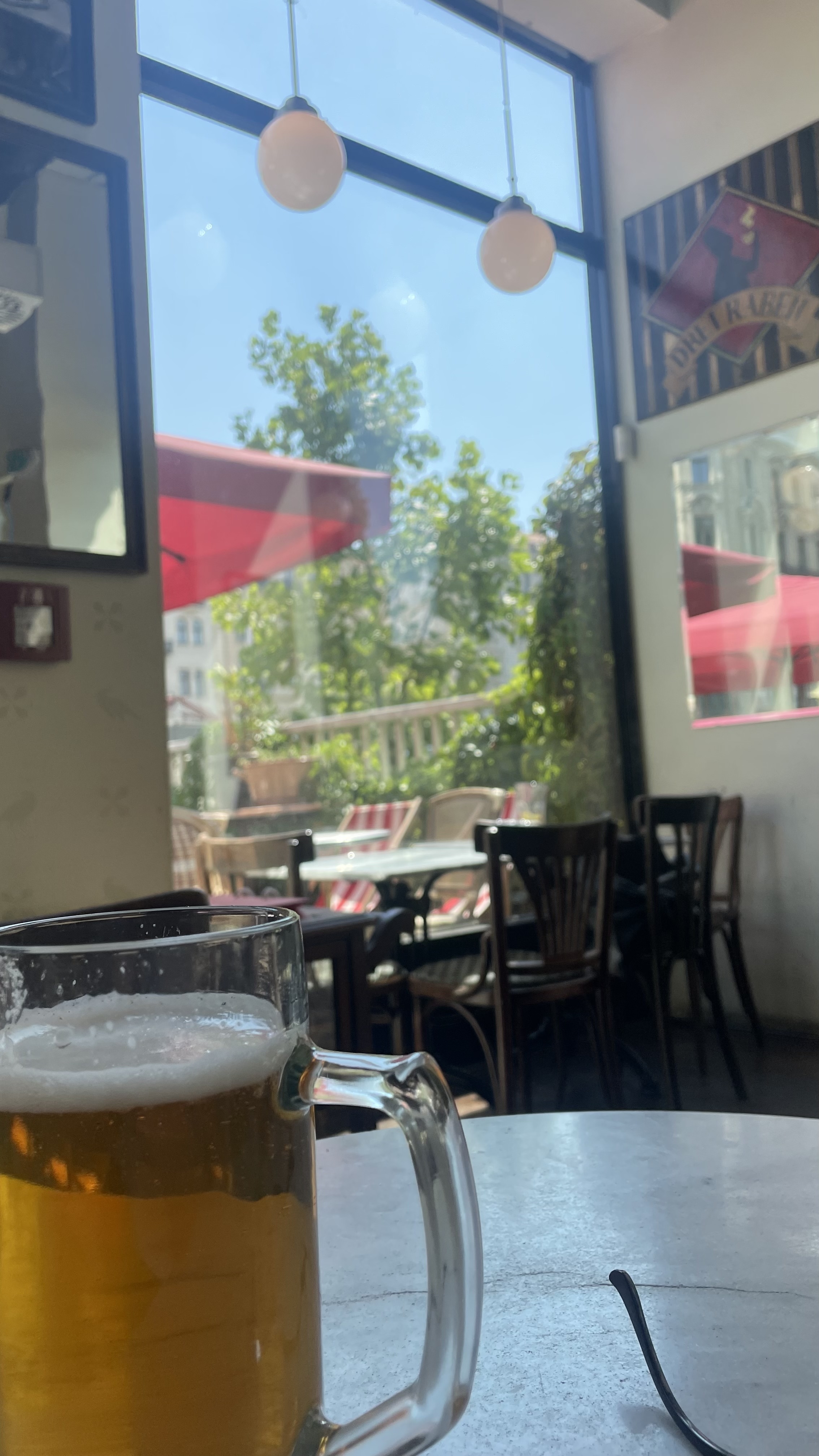 Sideways photo of a cafe table with an iced green drink, a sandwich, and an espresso cup, overlooking a sunny street