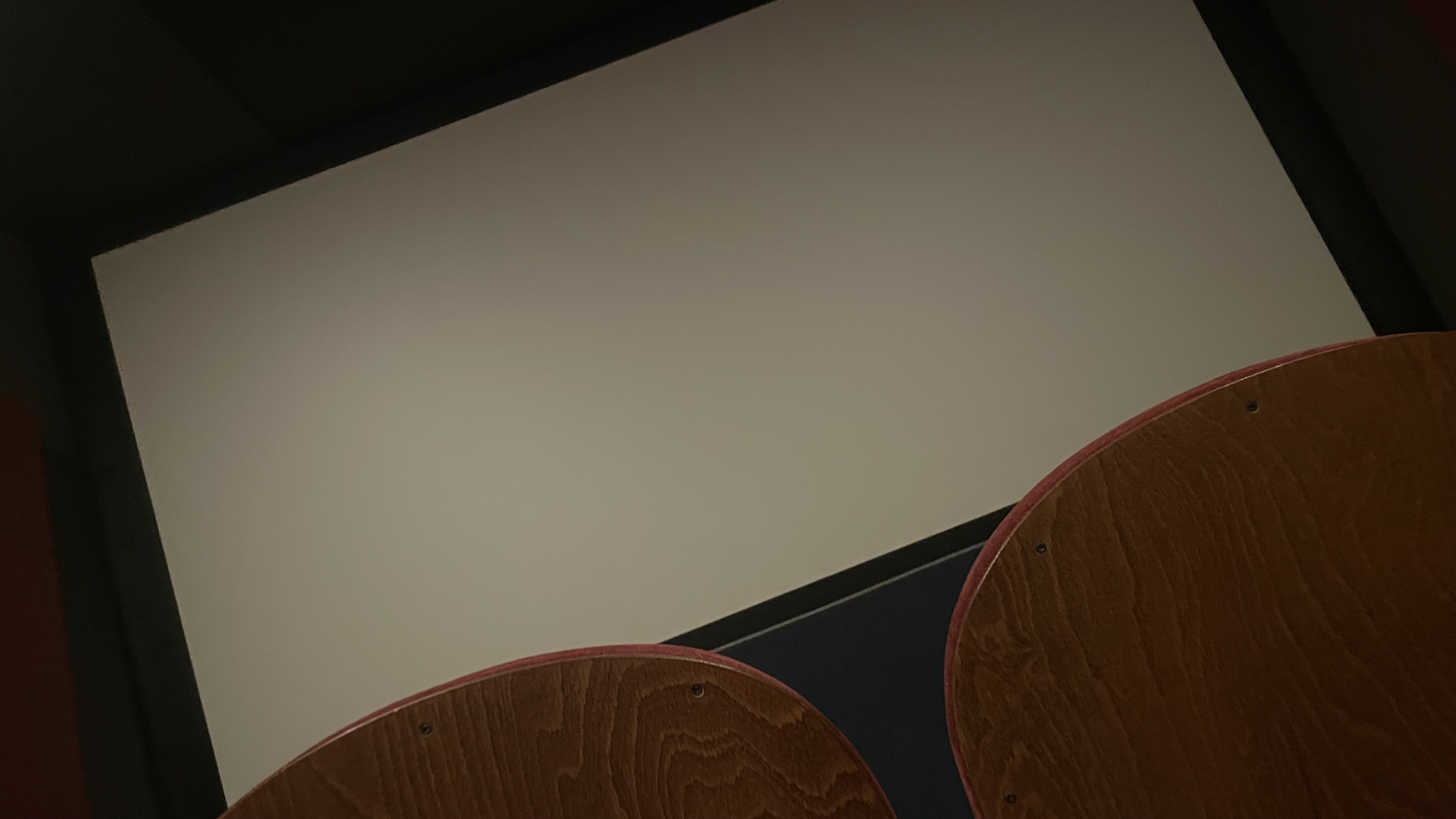 Dark, angled photo of a movie theater screen and wooden seat backs at Puskin cinema